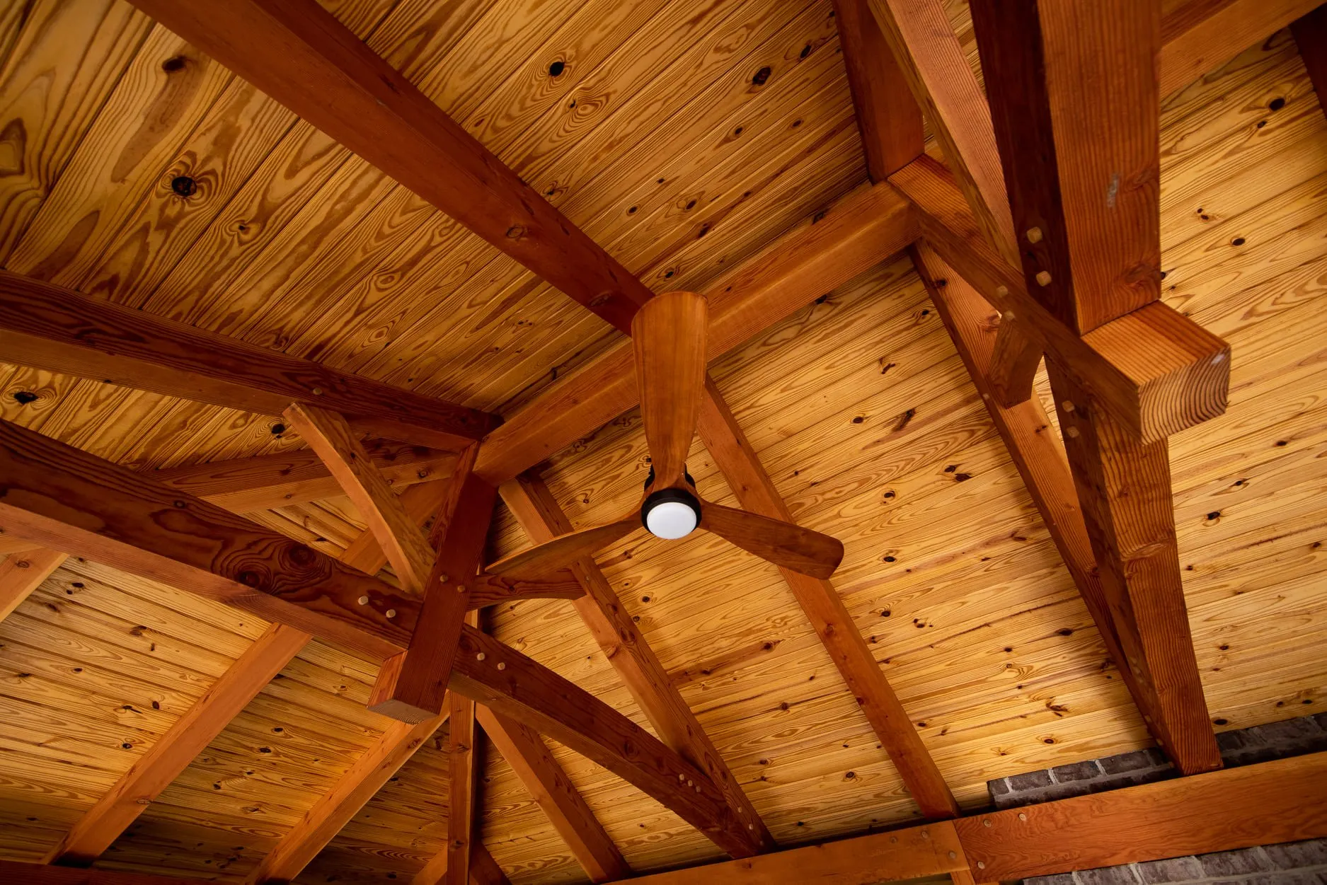 Exposed Beams: In a timber frame home, the structure is intentionally visible. Large beams, posts, and trusses are not hidden behind drywall—they define the space. These exposed structural elements create scale, rhythm, and architectural depth that cannot be replicated with decorative trim or faux beams. The frame becomes both the engineering system and the visual signature of the home.